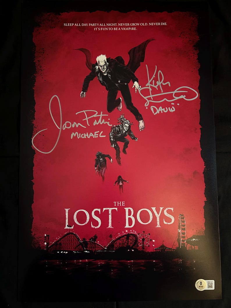 May include: A red poster for the movie "The Lost Boys" featuring the main characters in flight. The poster is signed by the actors, including Corey Feldman, Jamison Newlander, and Kiefer Sutherland. The text on the poster reads "Sleep all day. Party all night. Never grow old. Never die. It's fun to be a vampire."