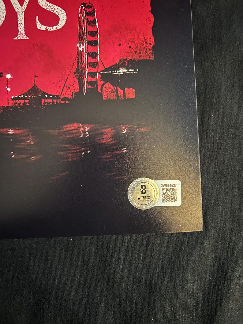 May include: A black and red poster with the word "BOYS" in white text at the top. The poster features a silhouette of a Ferris wheel and a cityscape in the background. The poster has a gold sticker with a QR code and the text "WITNESS AUTOGRAPH" in the bottom right corner.