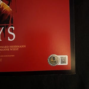 Op de afbeelding: Een rode filmposter met een zwarte rand. De poster toont een wolfachtig wezen met een bloederige bek en het woord "Days" in witte tekst. De poster bevat ook de namen "Edward Herrmann" en "Dianne Wiest" in witte tekst. Een zilveren sticker met een QR-code en de tekst "2W651497" bevindt zich in de rechterbenedenhoek.