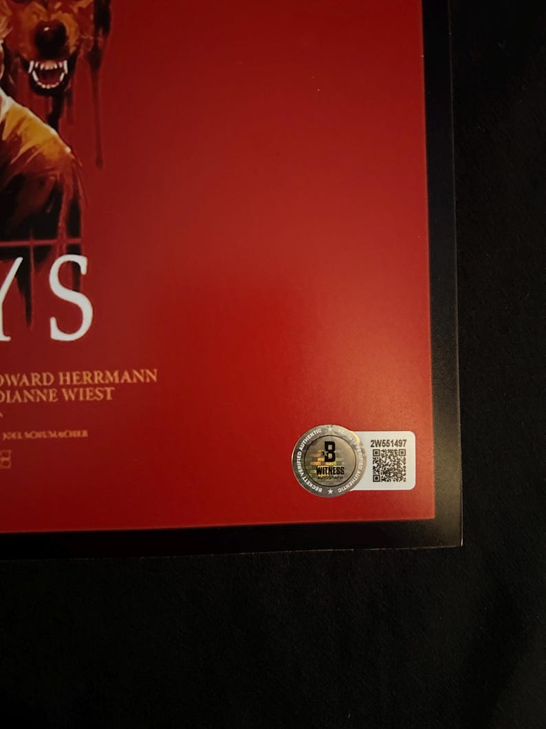 Op de afbeelding: Een rode filmposter met een zwarte rand. De poster toont een wolfachtig wezen met een bloederige bek en het woord "Days" in witte tekst. De poster bevat ook de namen "Edward Herrmann" en "Dianne Wiest" in witte tekst. Een zilveren sticker met een QR-code en de tekst "2W651497" bevindt zich in de rechterbenedenhoek.