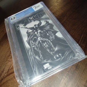 Può includere: Un fumetto classificato in una custodia di plastica. Il fumetto è Spawn #1 ed è classificato 9.0 da CGC. La copertina del fumetto presenta un'illustrazione in bianco e nero di Spawn, un supereroe con un mantello e catene.