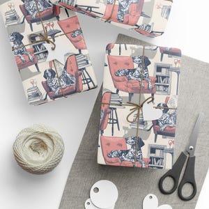 May include: Gift wrap with a repeating pattern of a dog in a red armchair, with books and wine glasses. The wrapped gifts are tied with twine and a heart-shaped tag. A ball of twine, scissors, and blank tags are also present.