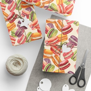 May include: Gift-wrapped boxes with a colorful macaron pattern. The boxes are tied with twine and adorned with white tags. A ball of twine, scissors, and additional tags are also present, suggesting a theme of gifting and presentation.