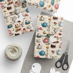 May include: Gift wrap featuring a repeating pattern of teacups, teapots, cakes, and macarons in shades of blue, pink, and beige. The wrapped gifts are tied with twine and have heart-shaped tags. A ball of twine, scissors, and blank tags are also visible.