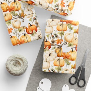 May include: Gift-wrapped presents with a pumpkin and autumn leaf pattern. The gifts are tied with twine and have blank tags. A ball of twine, scissors, and blank tags are also visible, suggesting a crafting or gift-giving theme.