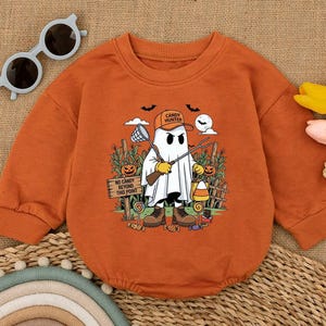 May include: Orange long-sleeved baby bodysuit with a Halloween-themed graphic. The graphic features a ghost character labeled "Candy Hunter" holding a net and a pitchfork. The design includes a cornfield, pumpkins, and the text "No Candy Beyond This Point."