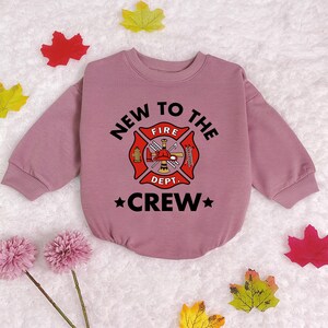 May include: A pink long-sleeved sweatshirt with a black graphic of a fire department logo and the text "New to the Crew".
