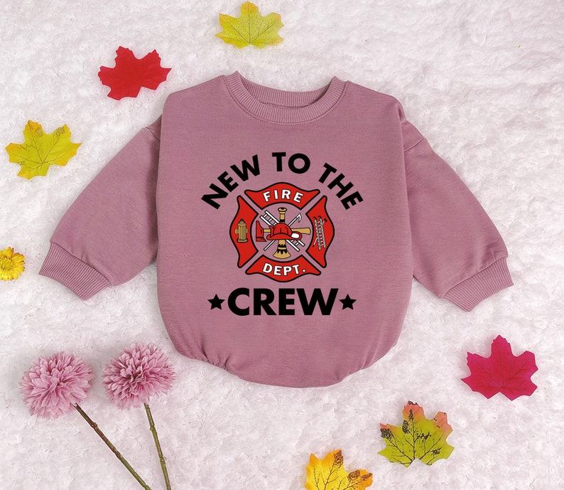 May include: A pink long-sleeved sweatshirt with a black graphic of a fire department logo and the text "New to the Crew".