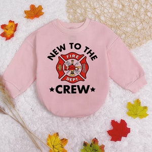 May include: Pink sweatshirt with a black graphic of a fire department logo and the text "New to the Crew".