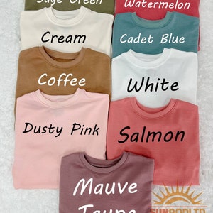 May include: A collection of folded crewneck sweatshirts in various colors, including sage green, cream, coffee, dusty pink, watermelon, cadet blue, white, salmon, and mauve taupe. Each sweatshirt has a color name printed on it.
