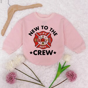 May include: Pink sweatshirt with a firefighter themed graphic that says "New to the Crew" with a fire department logo and a star on each side of the word "Crew".
