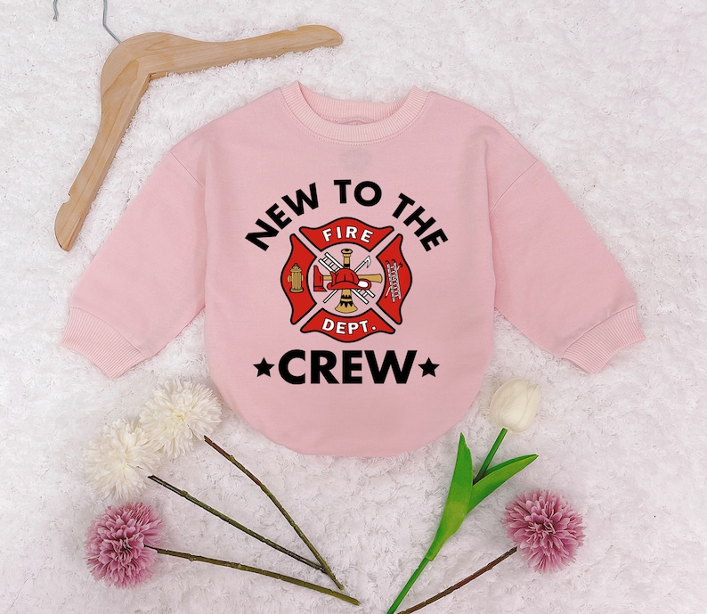 May include: Pink sweatshirt with a firefighter themed graphic that says "New to the Crew" with a fire department logo and a star on each side of the word "Crew".