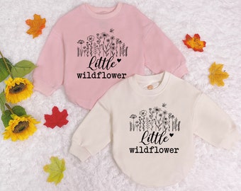 May include: Two pink and white long-sleeved shirts with a black floral design and the text "Little Wildflower" on the front.