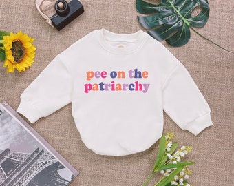 May include: White long-sleeve bodysuit with the text "pee on the patriarchy" in rainbow colors.