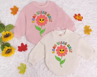 May include: Two pink and white sweatshirts with a colourful flower graphic and the text "Good Vibes Only".