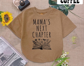 May include: A brown short-sleeved t-shirt with the text "Mama's Next Chapter" and a black and white illustration of a book with flowers.