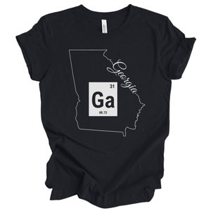 May include: Black t-shirt with a white outline of the state of Georgia and the cursive word "Georgia". A white box shows "Ga", number 31, and 69.72. The shirt is made of a soft material.