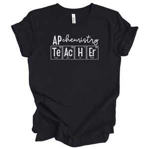 Puede incluir: Camiseta negra con las palabras "AP chemistry" sobre la palabra "TEACHER" deletreada con los elementos de la tabla periódica Te, Ac, H y Er. La camiseta está hecha de un material suave.