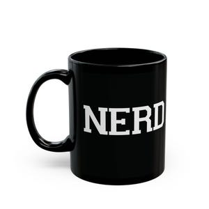 May include: A black ceramic mug with the white word "NERD" printed on the side. The mug has a curved handle and a glossy finish. The mug is designed for hot or cold beverages.