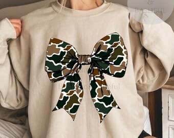 May include: A beige sweatshirt with a large camouflage bow printed on the front.