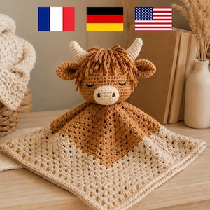 May include: A handmade crochet security blanket featuring a Highland cow design. The blanket is primarily tan and cream, with a brown cow head and horns. The blanket is square-shaped and has a textured, open weave.