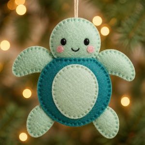 May include: A felt sea turtle ornament featuring a light mint green head and flippers with dark teal accents on the shell. The turtle has black bead eyes, a stitched smile, and pink circular cheeks, suspended by a thin string for hanging.