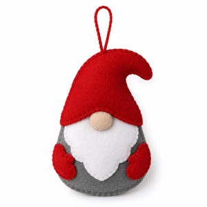 May include: A felt gnome ornament featuring a bright red pointed hat, a large white beard, a small beige nose, and a grey body. The gnome has two red mittens on the sides and a red string loop at the top for hanging. The edges are stitched.