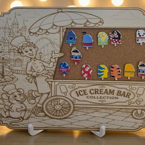 May include: A rectangular wooden display board featuring an engraved illustration of a chef and a mouse at an ice cream cart. The cart has a cork section displaying twelve colorful ice cream bar pins. The text ICE CREAM BAR COLLECTION is engraved.