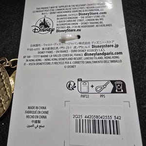 Puede incluir: Una etiqueta de producto blanca con el logotipo de Disney y texto en varios idiomas. La etiqueta incluye un c&oacute;digo de barras, s&iacute;mbolos de reciclaje y el texto "HECHO EN CHINA".