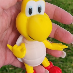 May include: A yellow and white toy turtle with red shoes. The turtle has a white shell and a yellow head with black eyes.