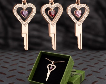 Collar con colgante de llave en forma de jaula con forma de corazón en oro rosa y piedras preciosas.