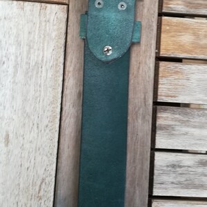 May include: A dark green leather belt with a silver buckle. The buckle has a simple design with two small holes on the top.