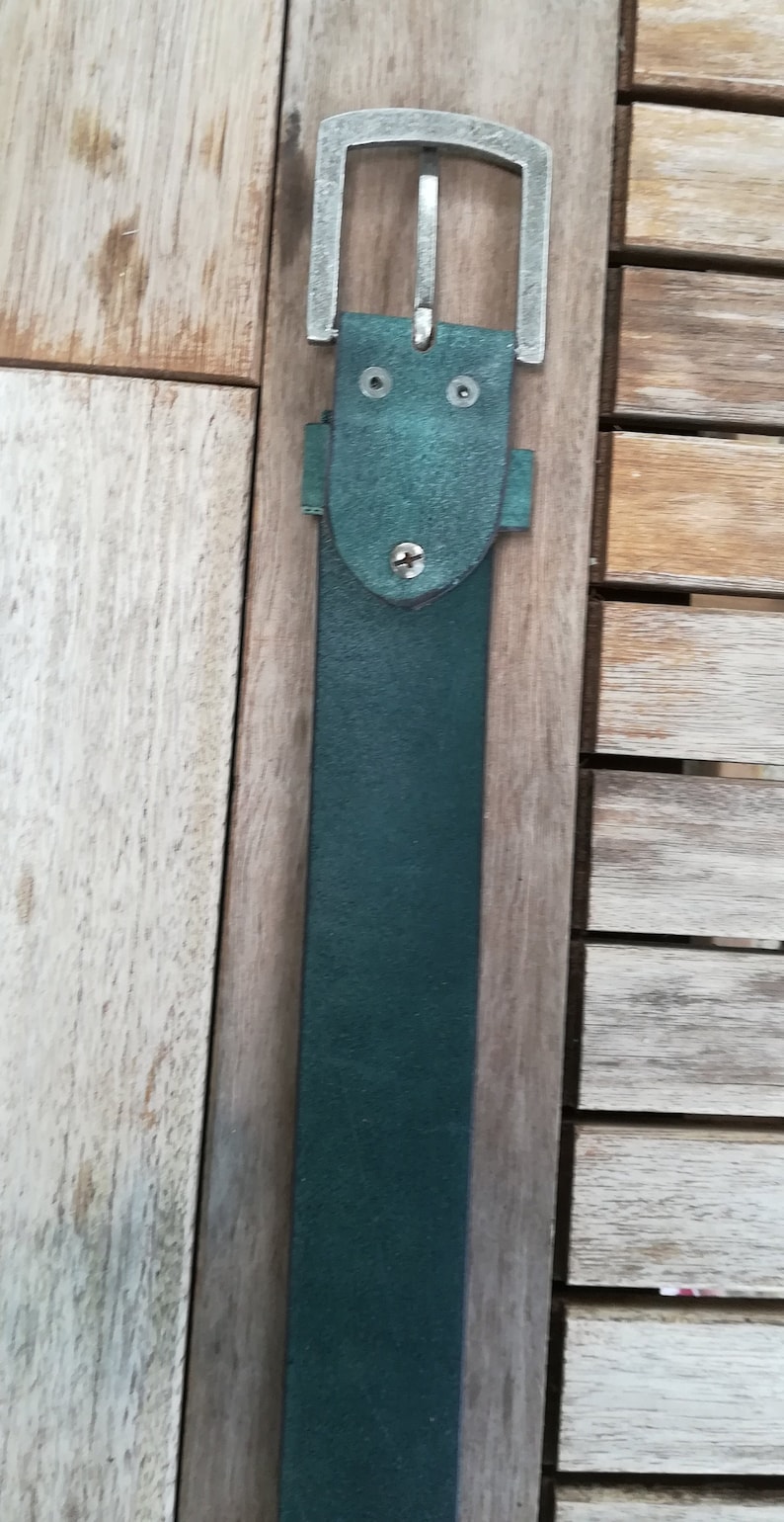 May include: A dark green leather belt with a silver buckle. The buckle has a simple design with two small holes on the top.