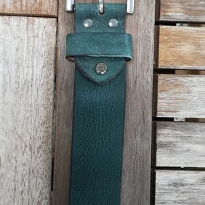 May include: A dark green leather belt with a silver buckle. The belt is on a wooden surface.