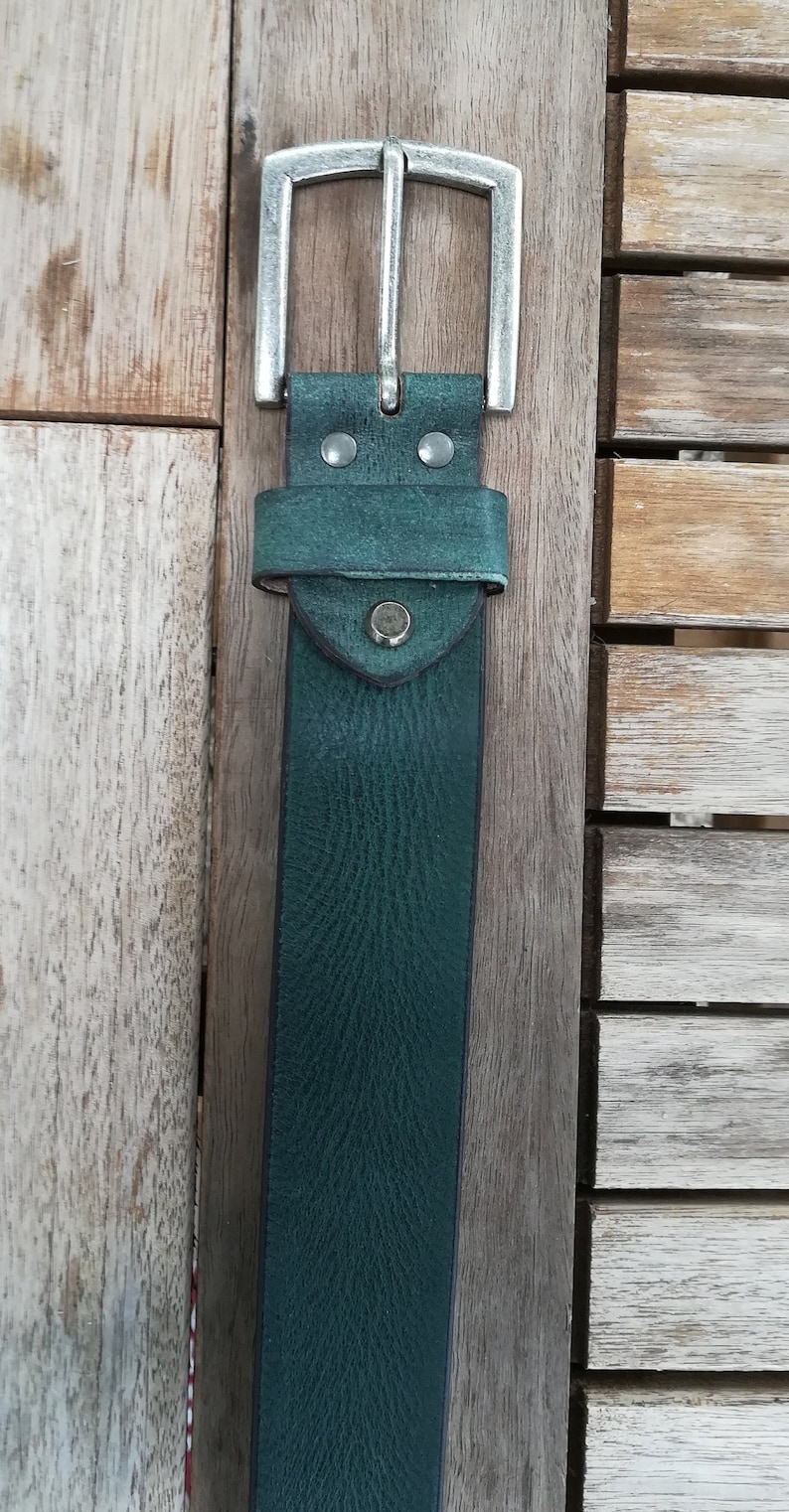 May include: A dark green leather belt with a silver buckle. The belt is on a wooden surface.