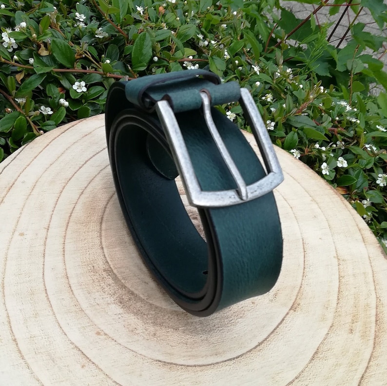 May include: A dark green leather belt with a silver buckle. The belt is rolled up and the buckle is visible.