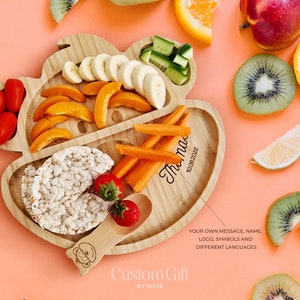 May include: A wooden divided plate shaped like a bear with a spoon. The plate has sections for different foods, such as fruit, vegetables, and rice cakes. The plate is personalized with the name "Thu na" and the date "10.08.2022".
