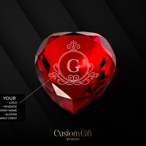 Puede incluir: Un pisapapeles de cristal rojo en forma de corazón con un monograma grabado en blanco de la letra "G" dentro de un marco decorativo. El texto "Custom Gift BY ROSS" está debajo del cristal.