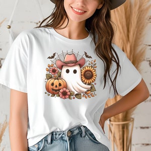 May include: White t-shirt featuring a graphic of a ghost wearing a pink cowboy hat and holding a pumpkin. The ghost is surrounded by sunflowers and autumn leaves.