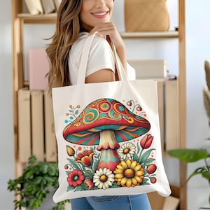 May include: A white canvas tote bag with a colorful psychedelic mushroom design. The mushroom is surrounded by flowers and leaves. The bag has a long handle.