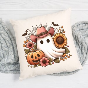 May include: A white ghost wearing a pink cowboy hat with a brown belt, surrounded by autumn foliage, a pumpkin, and sunflowers. The ghost has two black eyes and a friendly expression.