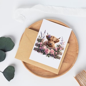 May include: A greeting card featuring a Highland cow with a floral crown peeking over a wooden fence with pink roses and purple lavender.