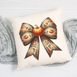 May include: A white cushion featuring a large, decorative bow made of green and cream ribbon with a small orange pumpkin in the centre. The ribbon has a floral pattern with small orange pumpkins.