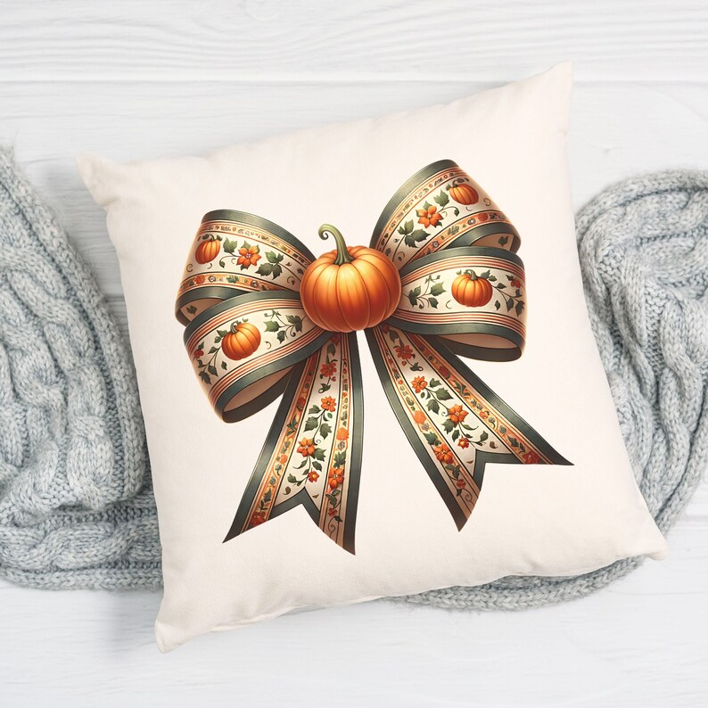 May include: A white cushion featuring a large, decorative bow made of green and cream ribbon with a small orange pumpkin in the centre. The ribbon has a floral pattern with small orange pumpkins.