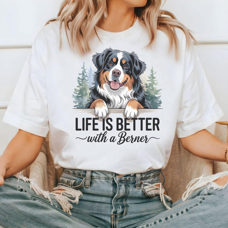 May include: White t-shirt with a graphic of a Bernese Mountain Dog peeking over a sign that reads "Life is better with a Berner".