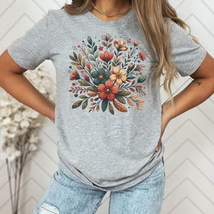 Peut inclure: Un t-shirt gris avec un imprim&eacute; floral repr&eacute;sentant un bouquet de fleurs orange, jaunes et turquoise avec des feuilles vertes.