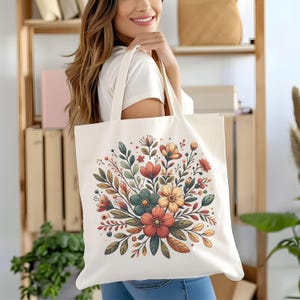 Peut inclure: Un sac fourre-tout en toile blanche avec un motif floral. Les fleurs sont dans des tons d'orange, jaune, rouge et vert. Le sac a deux anses.