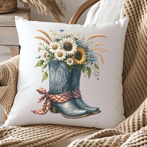 May include: A white square cushion with a watercolour illustration of blue cowboy boots filled with sunflowers, daisies, and wildflowers. A red and white checked ribbon is tied around the boots. The cushion has a rustic, country theme.