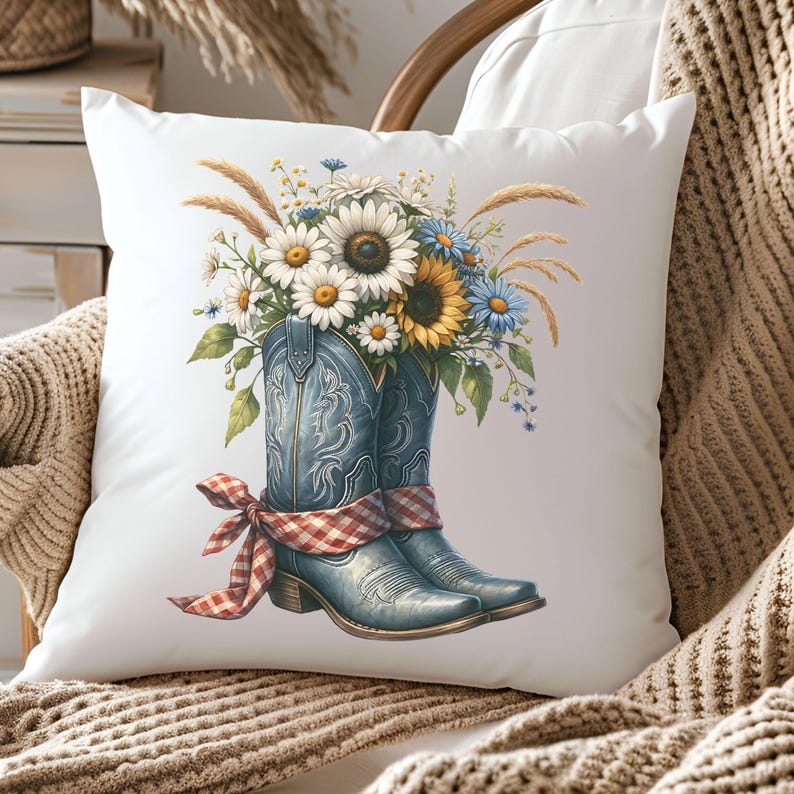 May include: A white square cushion with a watercolour illustration of blue cowboy boots filled with sunflowers, daisies, and wildflowers. A red and white checked ribbon is tied around the boots. The cushion has a rustic, country theme.
