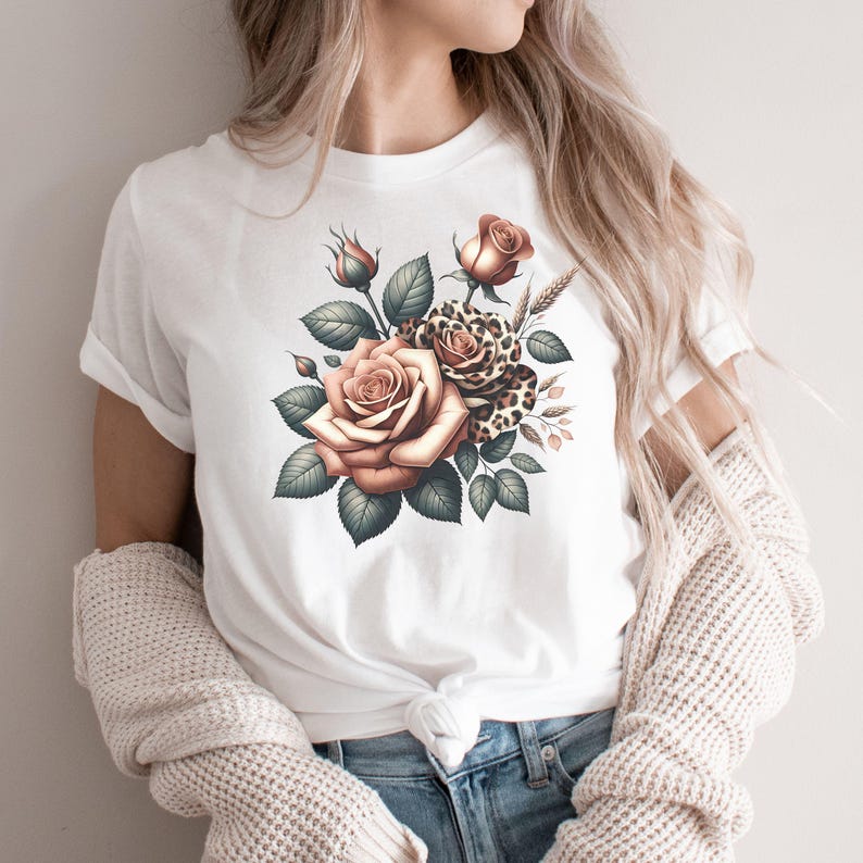 May include: White t-shirt featuring a floral design with roses in shades of peach and a leopard print accent. The design includes green leaves and wheat stalks. A stylish and feminine graphic tee.